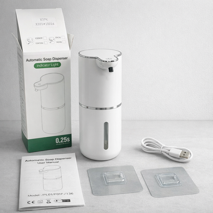 White automatic soap dispenser with packaging, USB cable, and user manual on a gray surface.